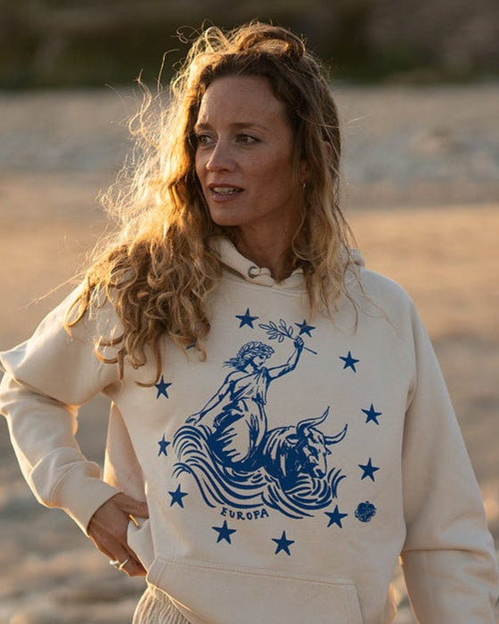 Frau am Strand im Ankerherz Hoodie EUROPA ONE LOVE Ivory Garment Dye, blauer Siebdruck Europa auf Zeus-Stier mit zwölf Sternen von Dani Garreton, Unisex Frontansicht